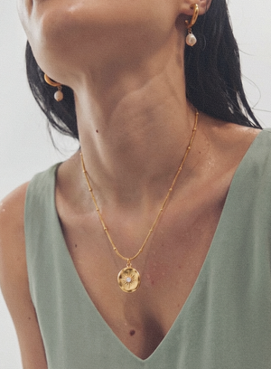 Gold-tone pendant necklace with round sunburst medallion charm worn on neckline