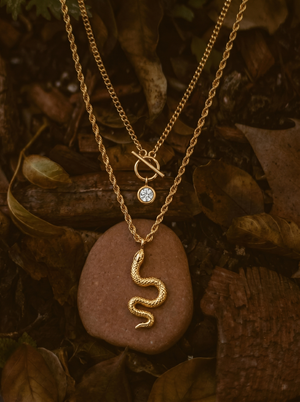 Gold-tone snake charm necklace with knot pendant and round crystal charm, layered chains