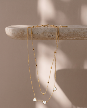 Gold necklace with heart pendants on a stone surface