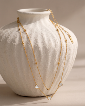 Gold necklace with heart-shaped pendants on a white vase
