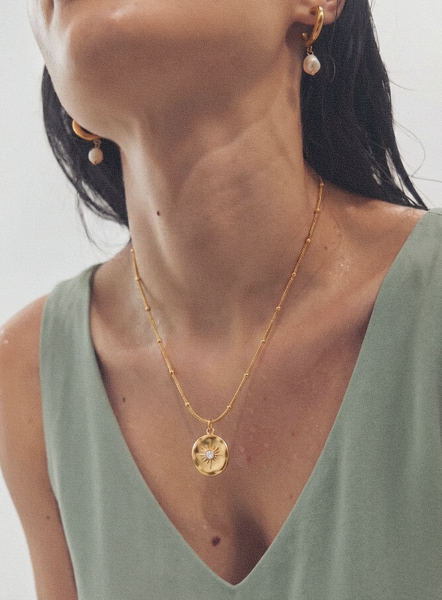 Gold-tone pendant necklace with round sunburst medallion charm worn on neckline