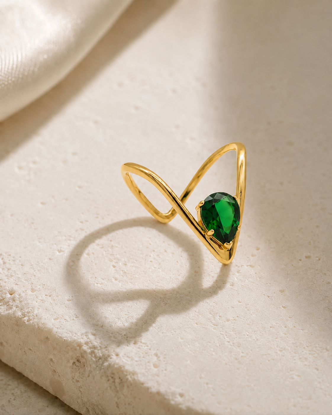 Gold-tone V-line solitaire ring with green oval gemstone, on light stone surface