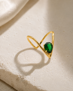 Gold-tone V-line solitaire ring with green oval gemstone, on light stone surface