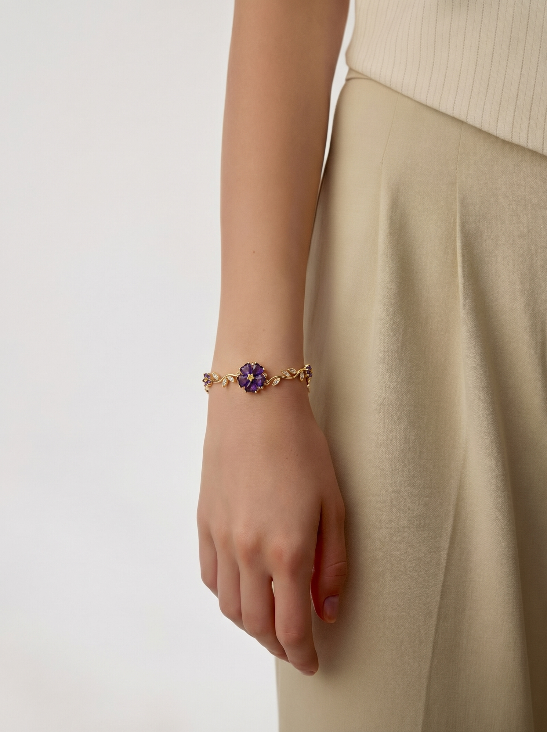 Gold bracelet with small purple flower charms on wrist, thin chain style