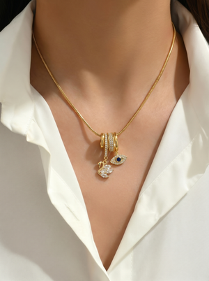Gold charm pendant necklace with blue evil-eye charm and swan drop, close to collar