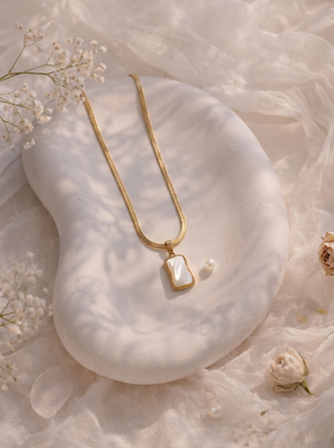 Gold necklace with a pendant on a white stone surface with delicate flowers.