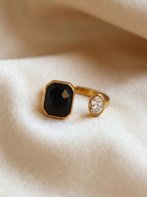 Gold ring with a black gemstone and a smaller clear gemstone on a beige fabric background
