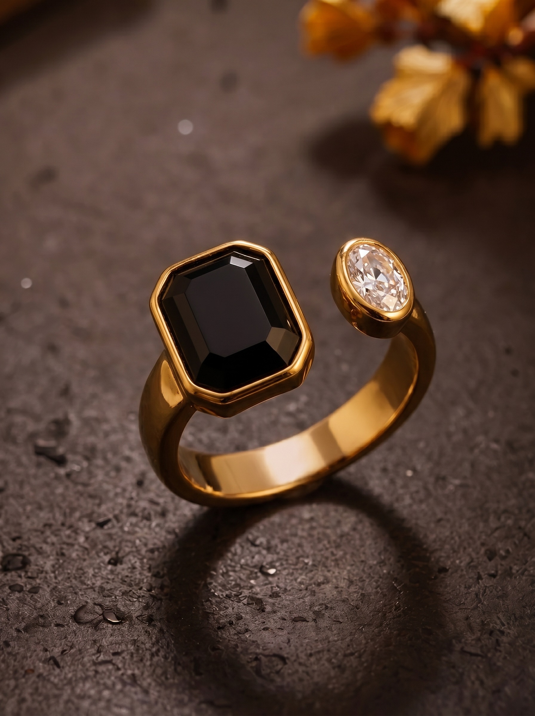 Gold ring with a black gemstone and a smaller diamond on a dark surface