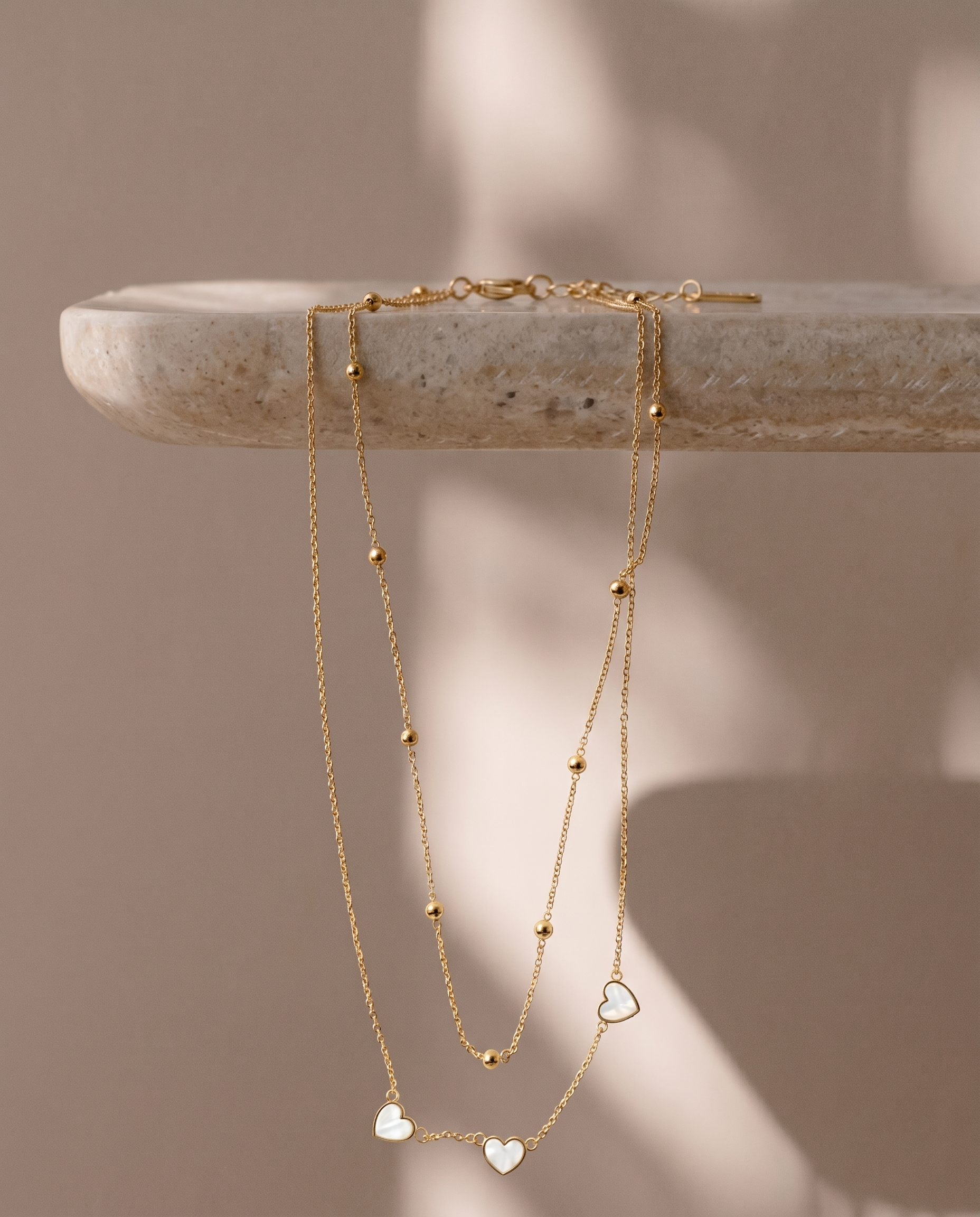Gold necklace with heart pendants on a stone surface