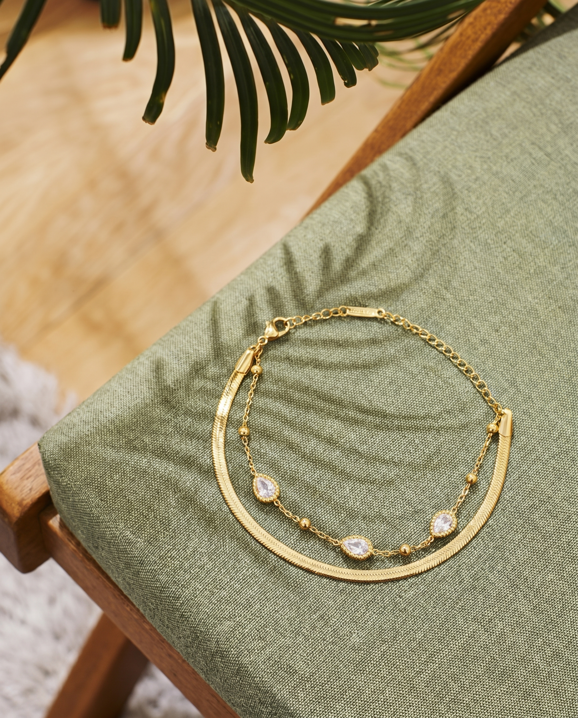 Gold layered chain bracelet with teardrop crystal charms and adjustable chain links.