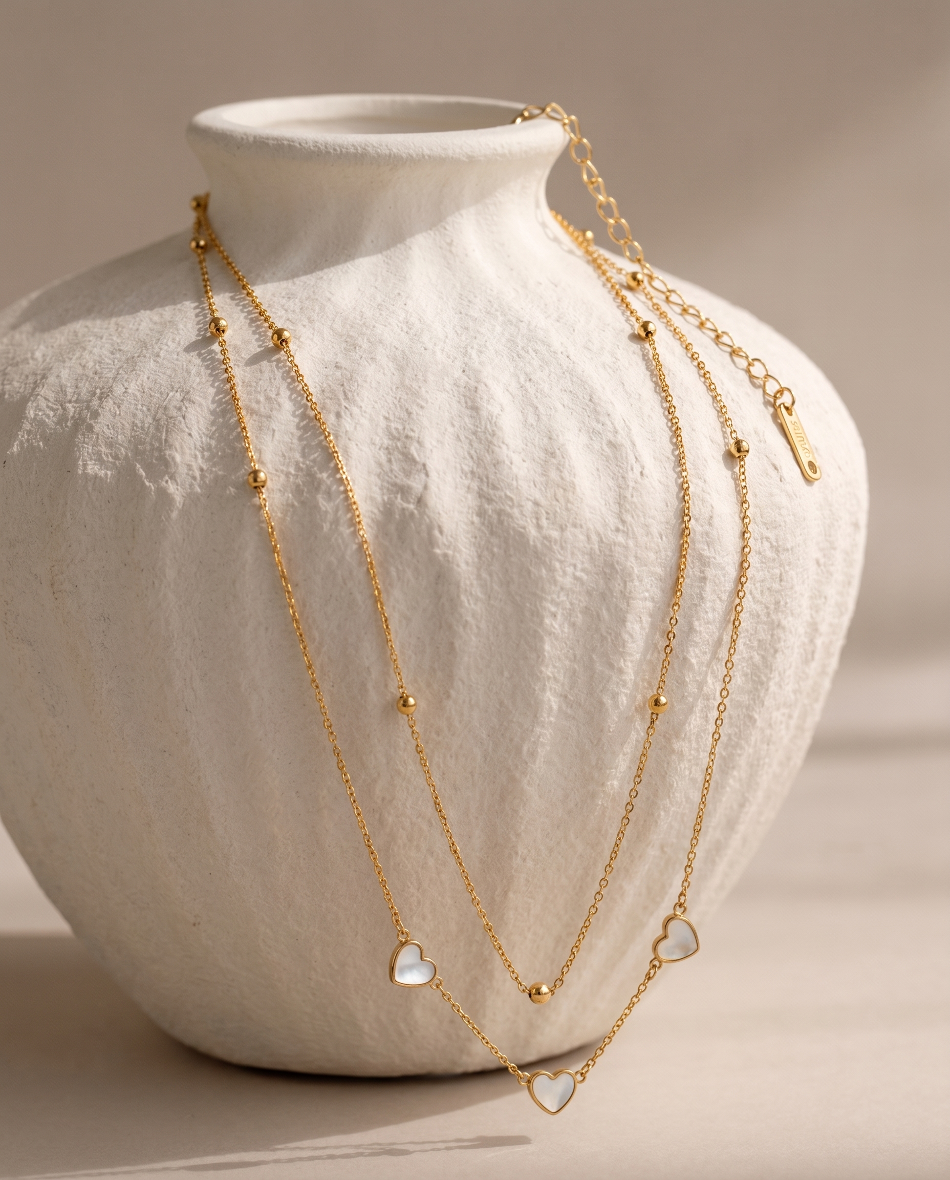Gold necklace with heart-shaped pendants on a white vase
