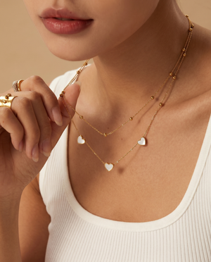 Close-up of a woman wearing a gold necklace with heart pendants on a beige background