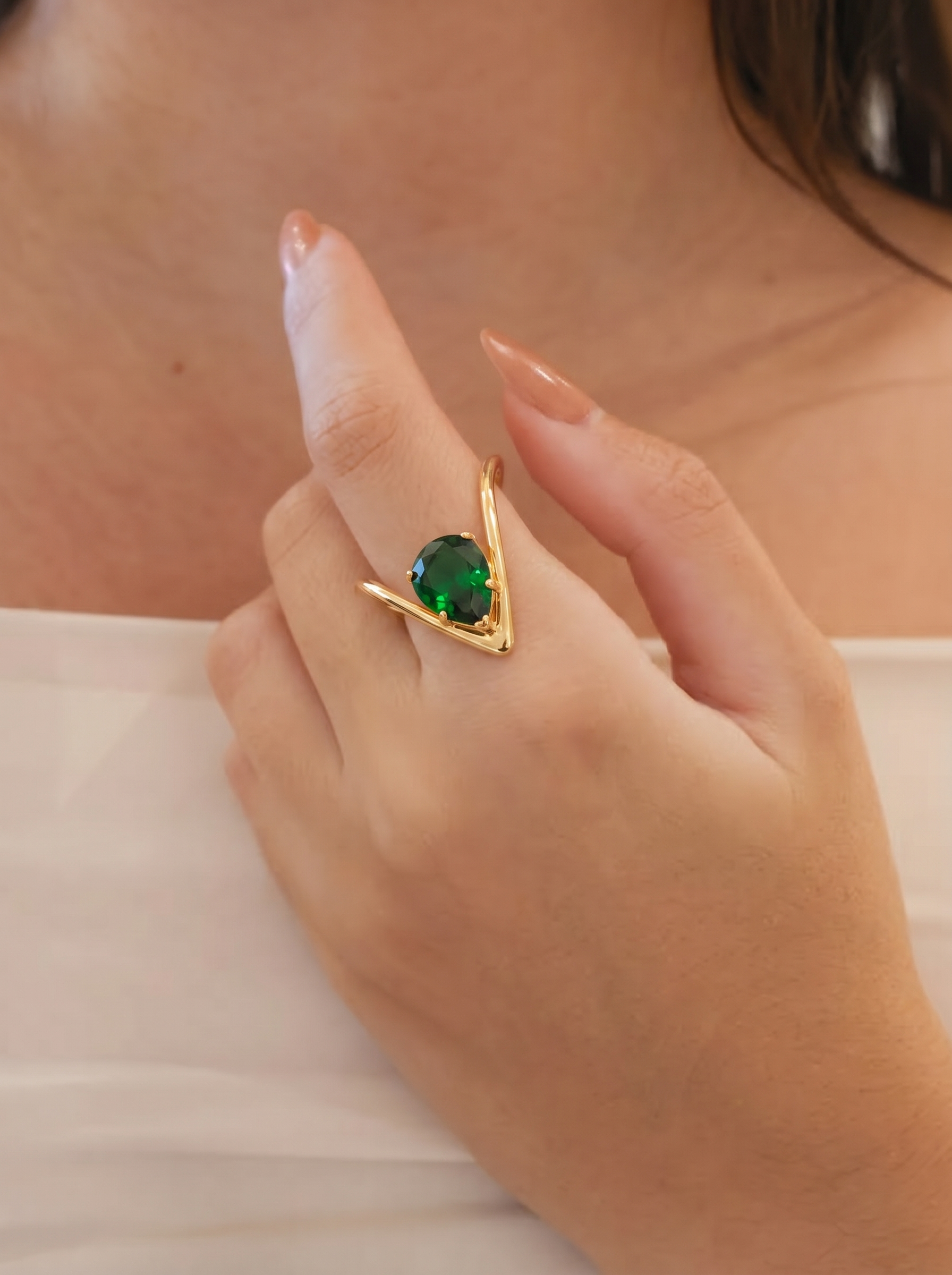 Gold-tone ring with green oval solitaire gemstone on an open V setting, worn on hand