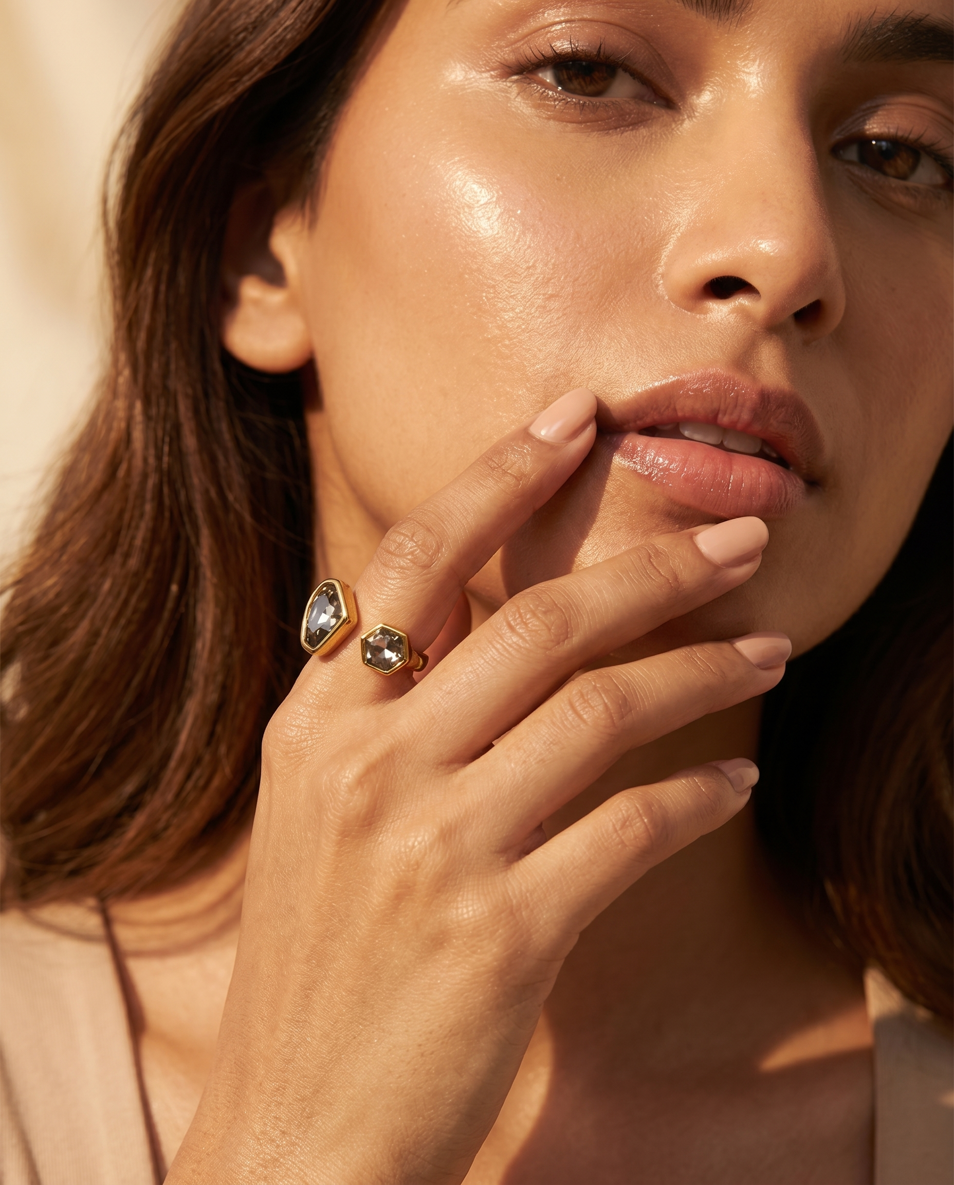 Close-up of a woman's hand with a gold ring featuring a green gemstone, touching her lips.
