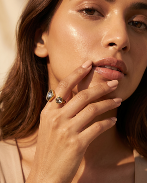 Close-up of a woman's hand with a gold ring featuring a green gemstone, touching her lips.