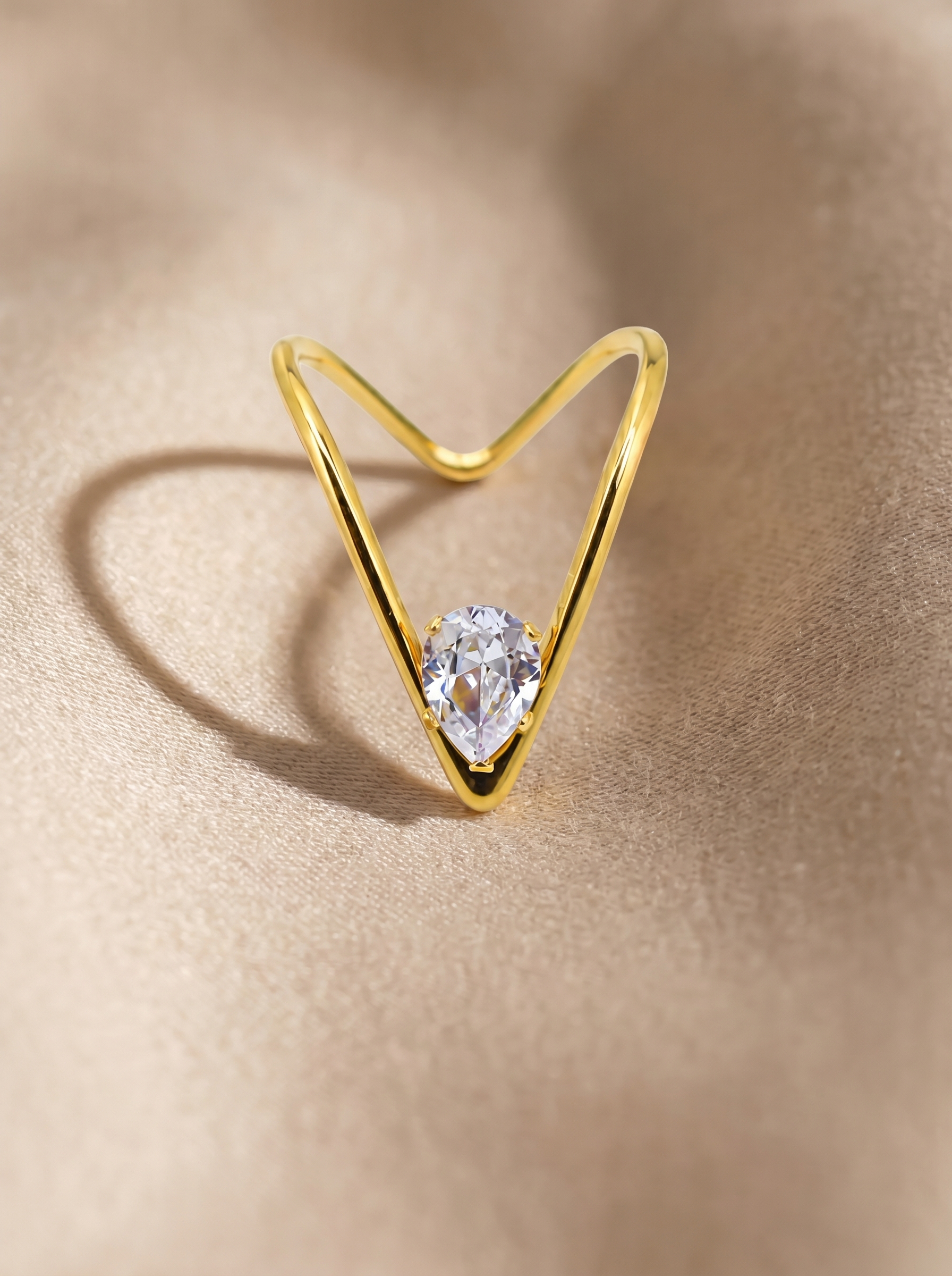 Gold open V ring with round clear gemstone on textured surface